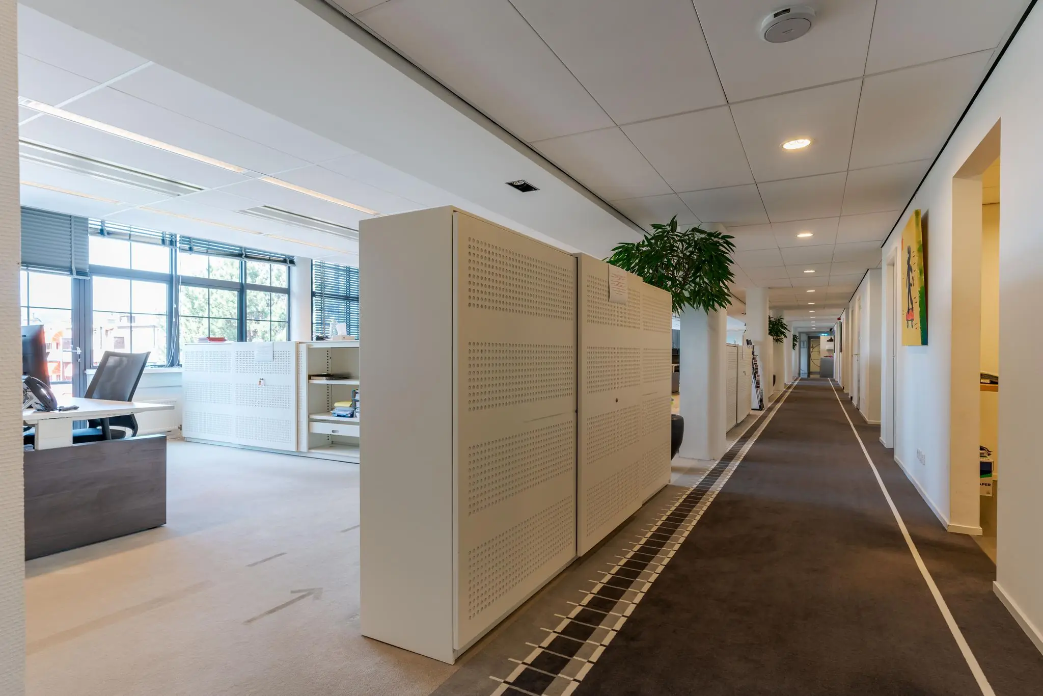 Modern kantoorinterieur aan de Van Alkemadelaan met open werkplekken, opbergkasten en een lange gang.